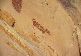 A Polynesian petroglyph of a kuri dog on a volcanic rock, with a tropical beach and outrigger canoe in the background.